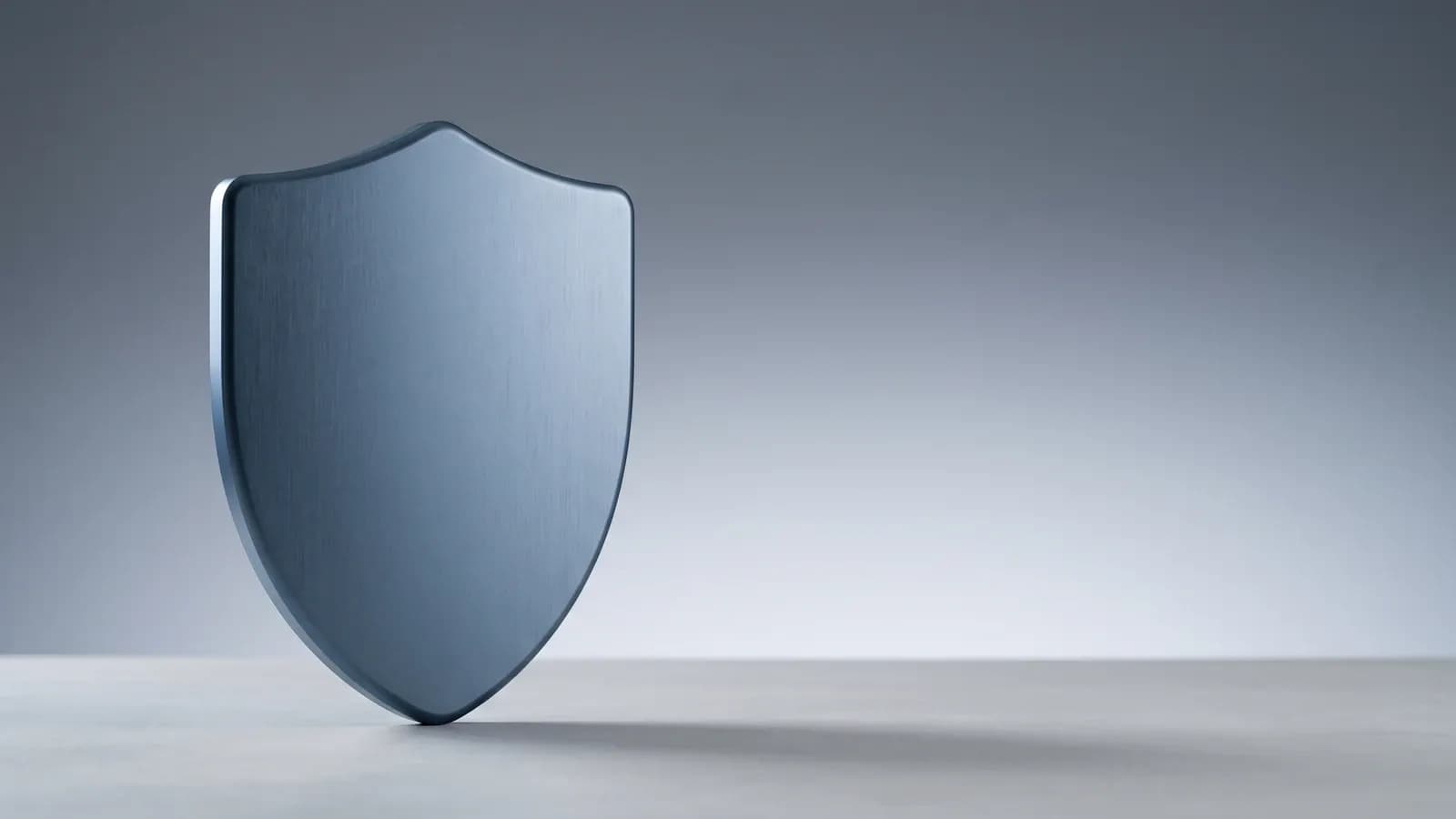 Bouclier en métal brossé bleu acier posé sur une surface claire, symbole de la protection intégrée de Windows Defender
