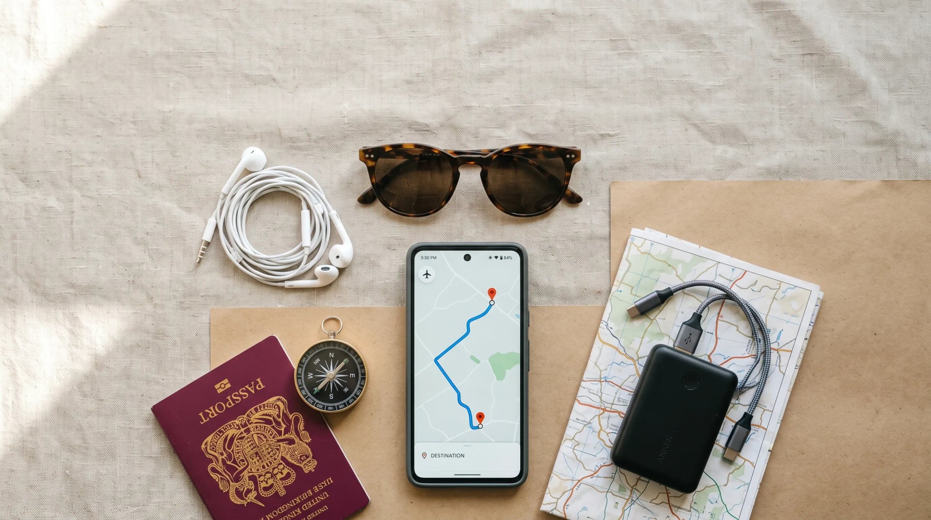 Smartphone posé au centre d'accessoires de voyage (passeport, batterie externe, carte papier) avec une carte hors-ligne à l'écran