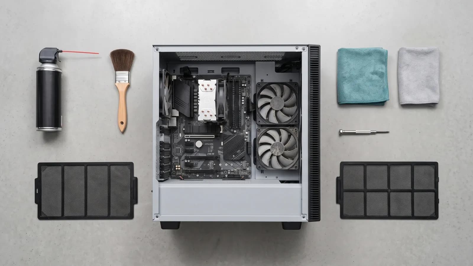 Vue de dessus d'un boîtier PC ouvert entouré du matériel de nettoyage aligné, bombe à air, pinceau, chiffons microfibre et filtres à poussière